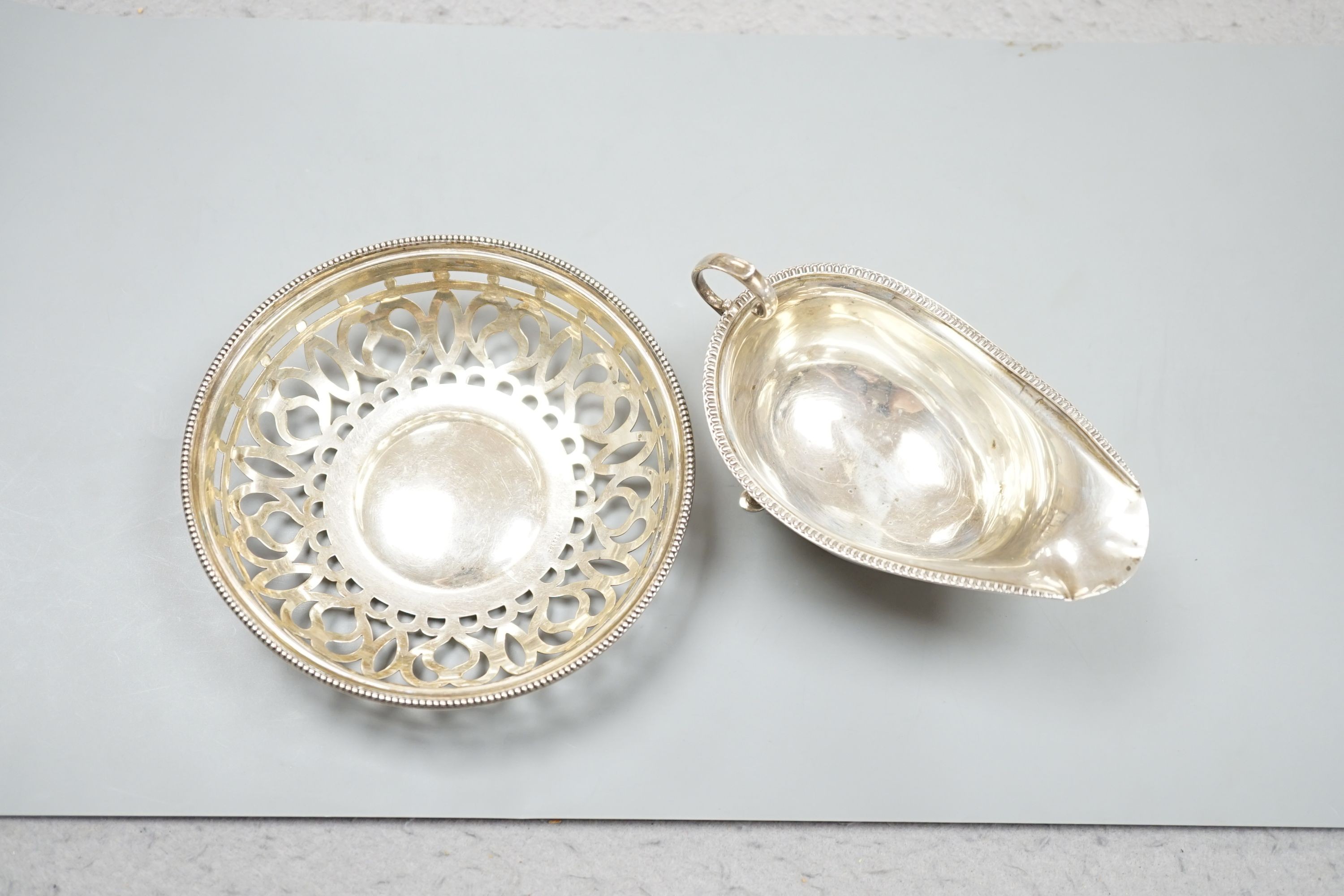An oval sauce boat with French gadroon rim and flying scroll handle, Birmingham 1918 and a pierced circular bowl with beaded rim, Birmingham 1910, diameter 15.25cm, 207 grams.
